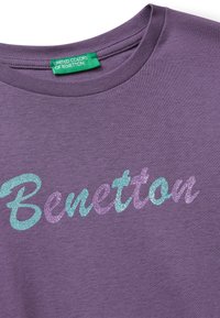 Lila Baumwoll-T-Shirt mit glitzernden türkis und lilac Buchstaben "Benetton". Klassisches Rundhalsdesign, glatte Textur.