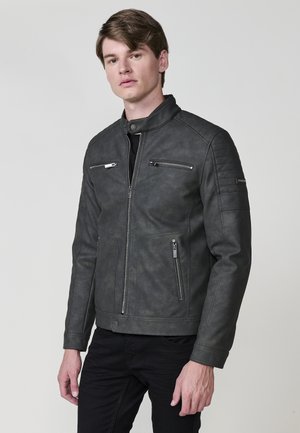 Chaqueta de hombre gris de cuero sintético con cuello alzado, bolsillos con cremallera, acentos acolchados en los hombros y un diseño ajustado.