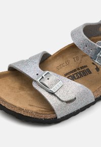 Sandali con glitter argento, dotati di due cinghie regolabili, fibbie in metallo argentato, soletta in suede e suola in gomma nera.