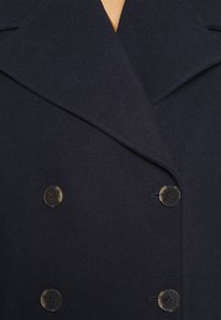 Manteau en laine bleu marine avec un design croisé, de grands revers et deux boutons noirs. Texture lisse sans motifs visibles.