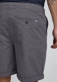 Grå shorts laget av lett stoff, med rullet kant, en knapp og lomme detaljer bak, samt elastisk midje.