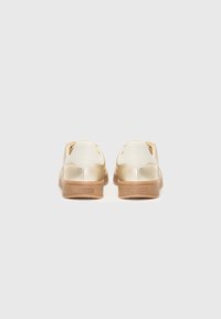 Gull og hvite sneakers med en glatt skinnøvre og en beige gummisåle. Bakfra som viser sømdetaljer og merkevarelogo.