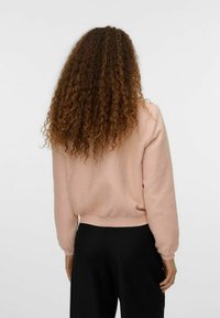Roosa tekstuuriga lühike sweatshird, millel on soonikkoes mansetid ja äär. Seljaview näitab volüümi täis varrukaid ja pehmet, mustrilist kangast. Mustad püksid on nähtavad.