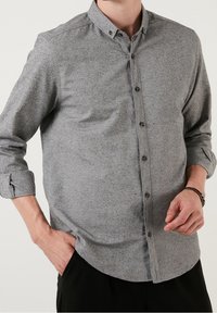 Grijs overhemd met knopen gemaakt van gestructureerde stof, uitgevoerd met een kraag, lange mouwen opgerold bij de manchetten en kleine ronde knopen.