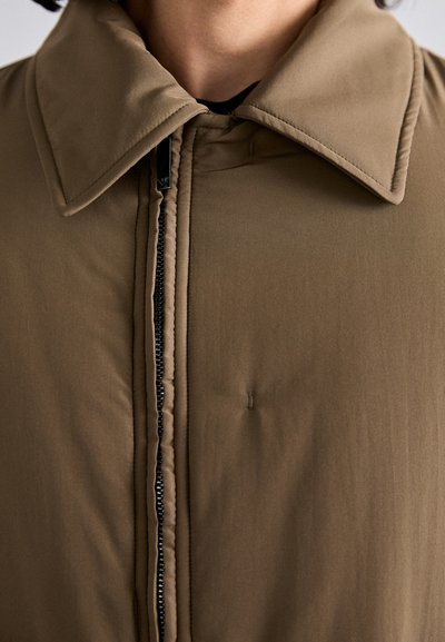 Chaqueta marrón con cremallera frontal, gran cuello, textura suave y sutiles detalles de costura, adecuada para climas moderados.