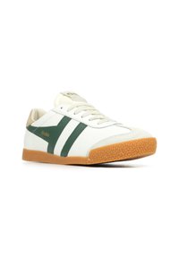 Zapatilla blanca con rayas y acentos verdes, suela de goma texturizada, parte superior de cuero suave y detalles cosidos en la punta.