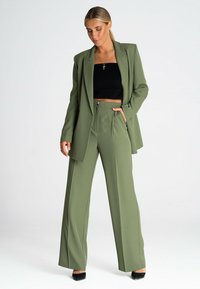 Oliwkowa, dopasowana marynarka oraz pasujące szerokie spodnie, o gładkiej fakturze i prostych liniach. Noszone na czarną bluzkę krótki.