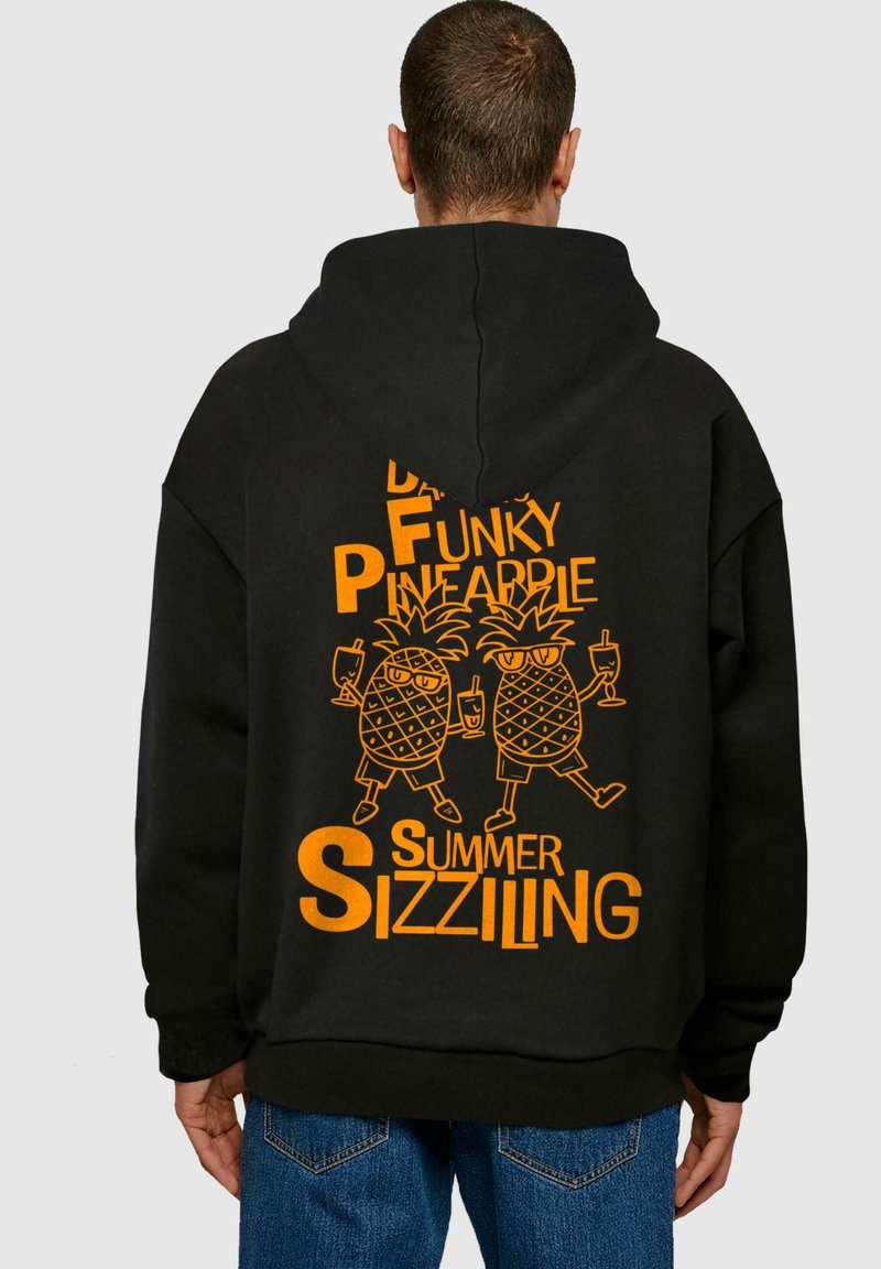 Fekete kapucnis pulóver narancssárga szöveggel és napszemüveget viselő, italokat tartó, rajzolt ananászokkal, amelyen a "Táncoló Funky Ananász Nyári Pezsgés" felirat szerepel.