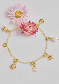 Bracciale in oro con vari ciondoli: una conchiglia con perla, una tartaruga rosa, cuori e fiori. Maglie texturizzate e accenti pastel.