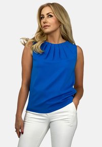 Niebieska bezrękawnikowa bluzka z plisowanym dekoltem, wykonana z gładkiego materiału. Zestawiona z dopasowanymi białymi spodniami, tworzącymi czysty, kontrastowy wygląd.