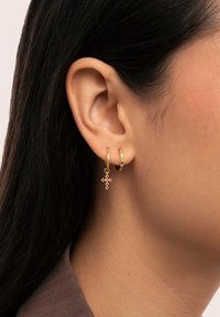 Orecchini a cerchio in oro con un piccolo ciondolo a croce rosa e accenti circolari con pietre multicolori. Superficie in metallo testurizzata visibile.