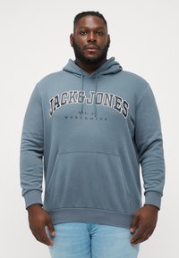 Gray hoodie made of soft fabric with a front pocket, featuring the text "JACK & JONES" in large white letters and drawstring on the hood.