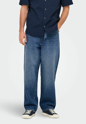 Løst siddende blå denimjeans med en falmet finish, der har et klassisk fem-lomme design og er parret med sorte sneakers.