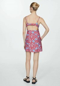 Rode bloemenjurk met blauwe accenten, spaghettibandjes, open rug en uitlopende rok. Gemaakt met zwarte sandalen met bandjes.