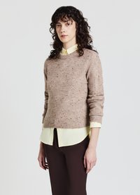 Braun gepunkteter Pullover mit einem gerippten Ausschnitt, kombiniert mit einem hellgelben Hemd mit Kragen und braunen enganliegenden Hosen.