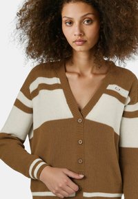 Cardigan strisce marroni e crema con scollo a V, texture a coste e chiusura con bottoni. Presenta un ricamo sul petto.