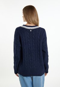 Dunkelblauer Strickpullover mit Kabelmuster, weiß gestreiftem Kragen und Knopfdetail im Rücken. Aus strukturiertem Woll-Mischgewebe gefertigt und mit lockerer Passform.