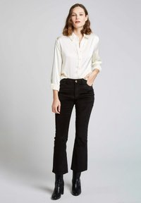 Chemisier blanc à boutons avec une texture lisse, associé à un pantalon en velours côtelé noir évasé et des bottines noires à talons.