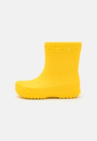 Botte en caoutchouc imperméable de couleur jaune vif avec des trous perforés près du haut et de la semelle, présentée sur le côté sur un fond blanc.