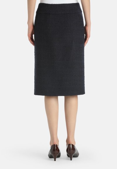 Woman wearing a knee-length dark textured skirt and brown low-heeled shoes, shown from behind against a white background.