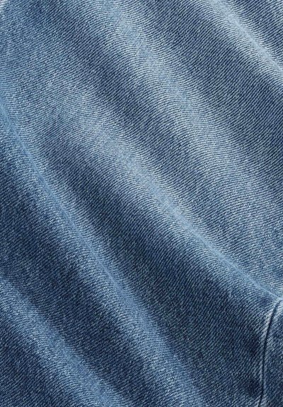 Gros plan sur un tissu en denim bleu clair montrant une texture de tissage diagonal et de doux plis créant des ombres délicates.