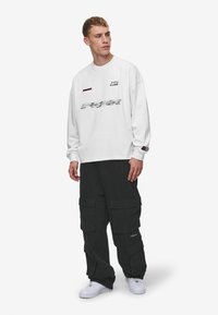 White long-sleeve shirt with front graphic and logo details, paired with black cargo pants featuring multiple pockets and loose fit.