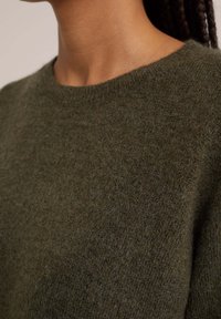 Olivgrön tröja med rund halsringning, mjuk textur och enkel design. Inga synliga mönster eller hårdvarudetaljer.