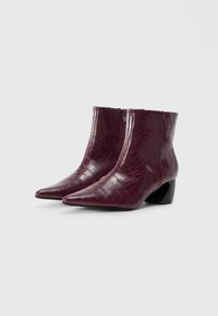 Stivaletti alti fino alla caviglia, di un oscuro bordeaux, con texture effetto coccodrillo, punte affusolate, cerniere laterali e tacco basso a blocco, su sfondo bianco.