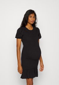 Vestido de maternidade preto feito de tecido texturizado. Apresenta um corpete justo, mangas curtas em balão e uma bainha com babados na altura da metade da coxa.