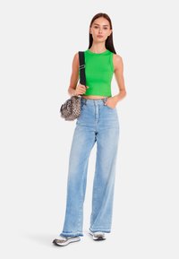 Green fitted crop top, light blue wide-leg jeans, animal-print bag, and sneakers with a mix of black and white accent colors.