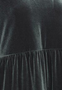 Svart sammetklänning med en slät övre del och samlad textur vid midjan. Mjuk lyster utan synliga mönster eller detaljer i metall.