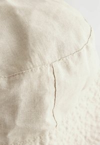 Chapeau seau en lin beige avec une surface texturée, des coutures visibles et une couronne arrondie. Matière légère adaptée aux temps chauds.