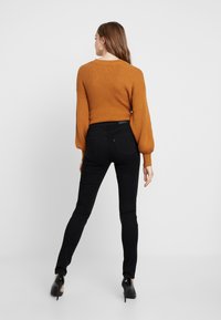 Pull en maille côtelée orange à manches ballon, associé à un jean skinny noir et des chaussures à talons hauts noires, vu de l'arrière.
