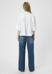 White shirt with short, wide sleeves and back yoke detail, paired with high-waisted, wide-leg blue denim jeans. Smooth texture.