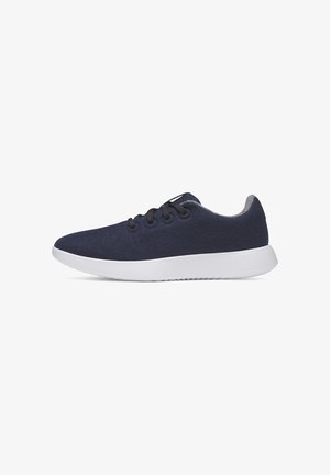 Sneaker blu navy con lacci neri e suola bianca, realizzata in tessuto morbido, mostrata di lato su sfondo bianco.