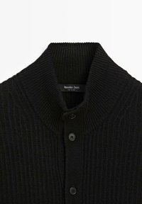 Černý žebrovaný kardigan s vysokým límcem, který má na přední straně tři černé knoflíky a štítek s nápisem "Massimo Dutti."
