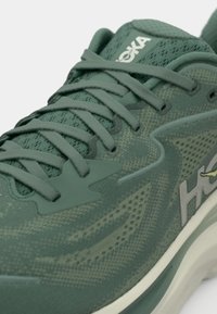 Grüner Sportschuh mit Obermaterial aus Mesh und Synthetik, Schnürdesign, gepolstertem Kragen und Logodetail, mit strukturierter Oberfläche und Gummisohle.
