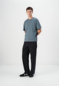 Tricou gri cu mânecă scurtă asortat cu pantaloni largi negri și adidași negri, având un design simplu și o croială lejeră.