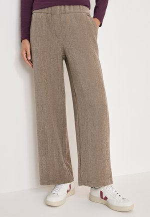 Bruine, gestructureerde wijde broek met een hoge elastische tailleband en zijzakken, gecombineerd met witte sneakers met rode accenten.