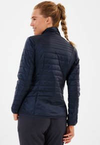 Marineblå peacoat med høj krave, der har horisontale quiltede linjer og en glat tekstur. Tætsiddende design med lange ærmer.