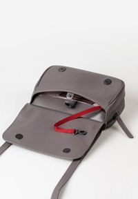 Borsa a tracolla grigia in pelle con chiusura a patta, dotata di una tracolla rossa, tasca interna con zip e bottoni a pressione neri. Texture liscia.