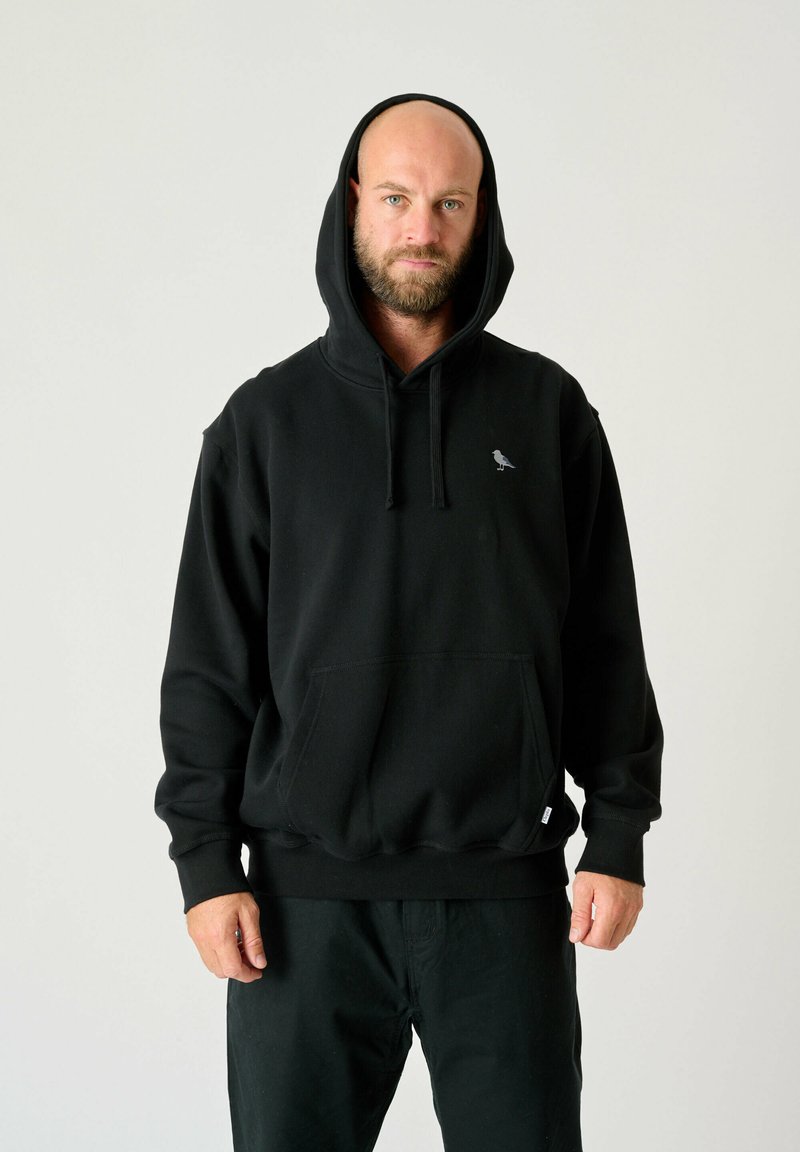 Black hooded sweatshirt made of soft fabric, featuring a front pocket and a small bird logo on the left chest area.
