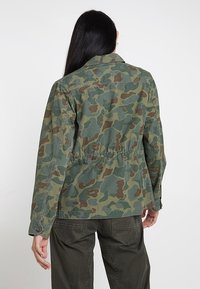 Veste de camouflage à manches longues, avec une taille à cordon et des poignets boutonnés. Fabriquée en tissu léger dans des tons de vert et de marron.