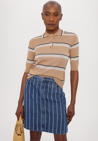 Polo shirt en tricot beige avec des rayures bleu marine et bleu clair, associé à une jupe en jean avec des rayures blanches verticales et une fermeture à boutons sur le devant.
