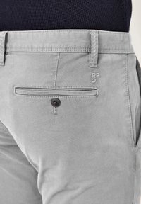 Close-up of light gray pants back pocket with button and belt loops, worn with dark knit top.