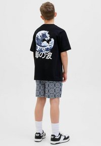 T-shirt nera con un design di onde blu e testo giapponese sul retro, abbinata a pantaloni corti blu a fantasia e scarpe da ginnastica nere.