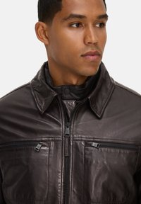 Bruine leren jas met een rits aan de voorkant, drukknoopkraag en twee ritszakken. Heeft een soepele textuur en een gestructureerd ontwerp.