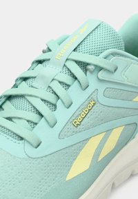 Sneaker w kolorze akwamarynowym wykonany z siateczki i materiału syntetycznego, z żółtymi akcentami, zaokrąglonym noskiem, grubą podeszwą i płaskimi sznurowadłami. Obecne logo Reebok.