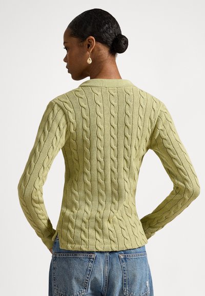 Svetlo zelena pulover iz kabelskega pletenja z oprijetim krojem, dolgimi rokavi in klasičnim ovratnikom, kombiniran z jeans hlačami.