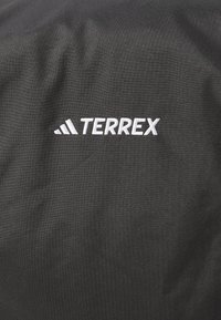 Black fabric with a smooth texture featuring a white "TERREX" logo, positioned on the upper section, with a subtle sheen.